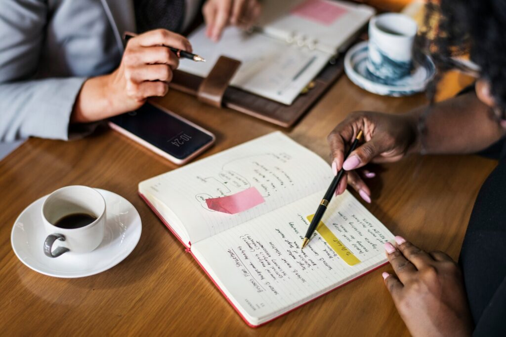 Duas pessoas se reunindo para pesquisas de satisfação em uma mesa e debatendo sobre dados escritos em um caderno